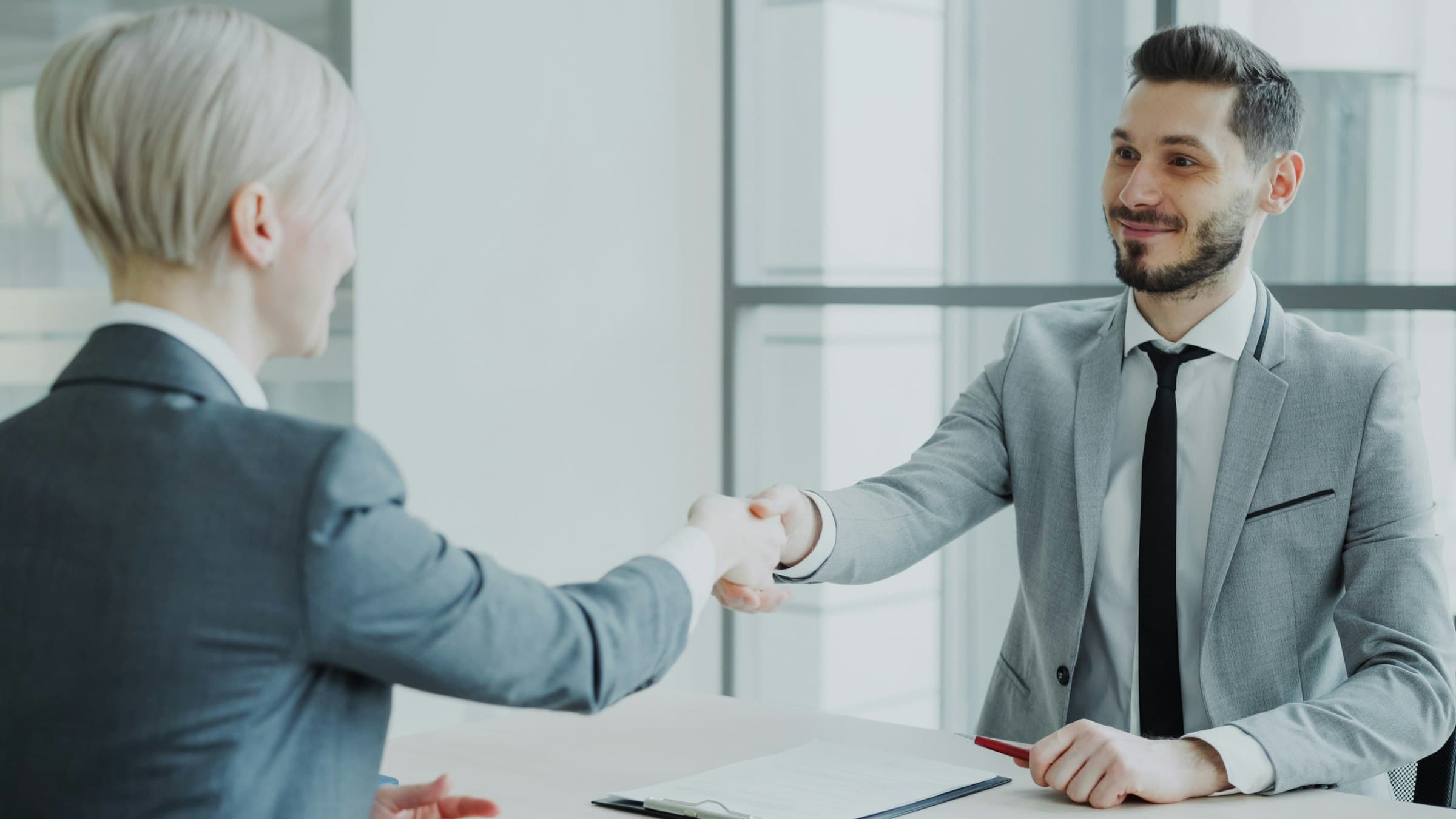 A hiring manager in a suit shaking hands with a job candidate across a table after a successful interview