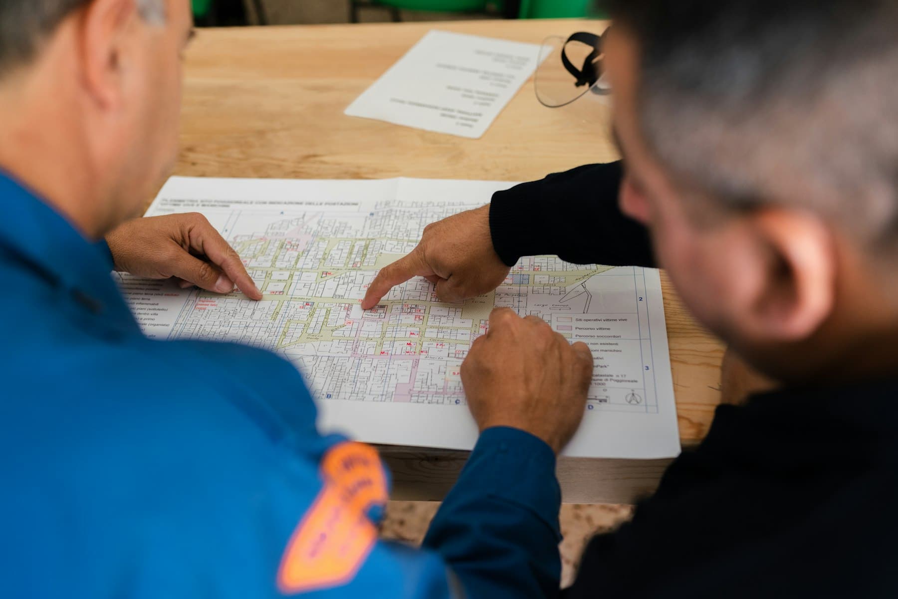 Two structural engineers in high-visibility vests reviewing a site map together